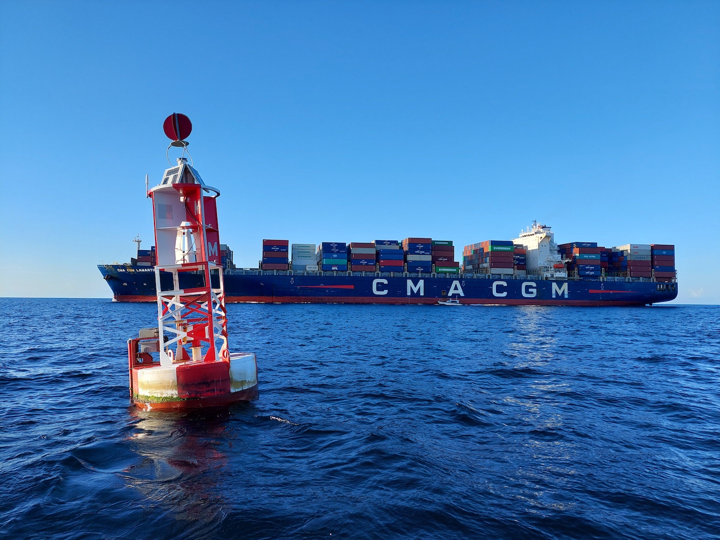 Buoy in Ocean with view of cargo ship in background that is pulling into Miami Harbor .